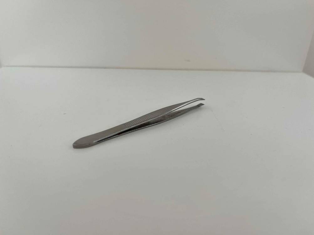 Im Test: silberne Pinzette liegt auf weißer Fläche.