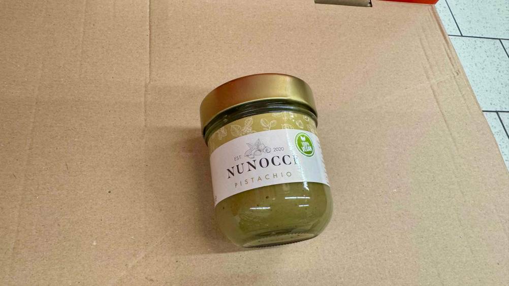 Ein Glas der getesteten Pistaziencreme liegt auf einem Karton.