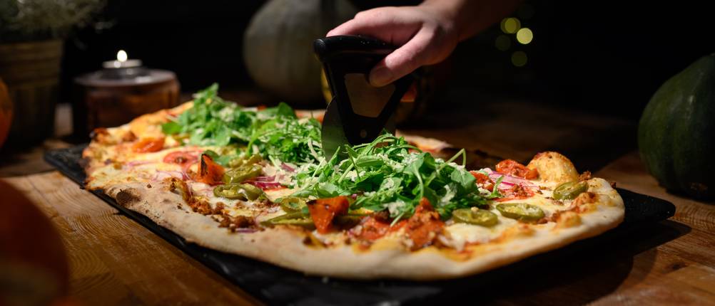 Pizza wird mit einem Pizzaschneider geschnitten.