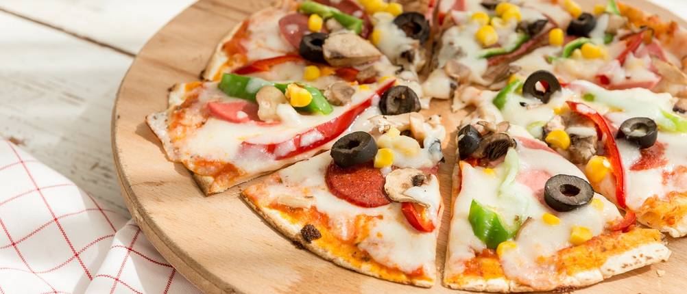 Eine dünne Pizza liegt geschnitten auf einem Holzbrett.