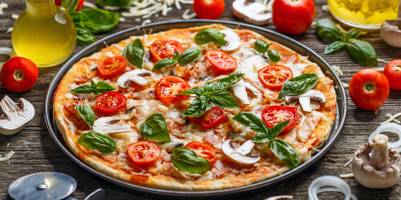 Fertig gebackene Pizza liegt auf einem runden Pizzablech.
