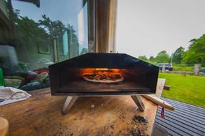 Pizzaofen getestet: Mobiler Pizzaofen mit Pizza steht auf einem Tisch auf einer Terrasse vor einem Haus.