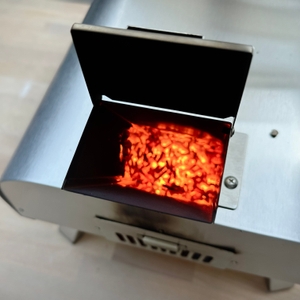 Die geöffnete Brennkammer des Big Horn Outdoors SRPG18003 zeigt glühende Pellets. Ein Metallgriff ermöglicht das Nachfüllen.