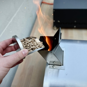 Pellets werden während aktiver Flamme in den Brennkanal des Big-Horn-Outdoors-SRPG18003-Pizzaofens nachgefüllt.