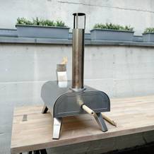 Der Big Horn Outdoors SRPG18003 steht einsatzbereit auf einem Tisch im Außenbereich. Die Flamme und der Kamin sind deutlich sichtbar.