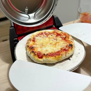 Eine fertige Pizza aus dem G3Ferrari Pizzaofen wird auf einen Teller gelegt.