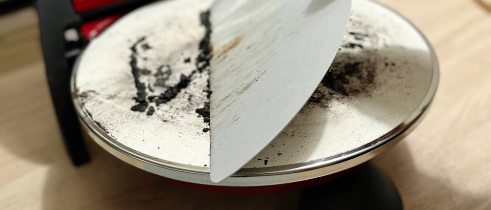 Mithilfe eines Schabers werden die Reste einer Pizza vom G3Ferrari Pizzaofen abgekratzt.