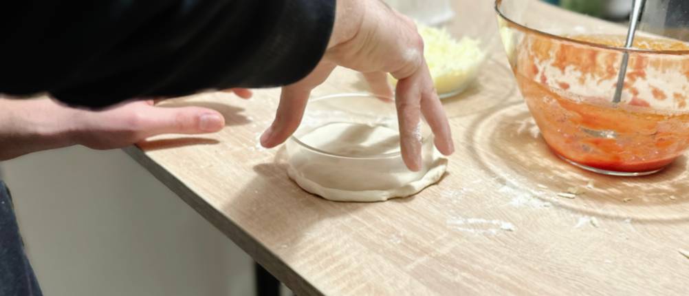 Jemand bereitet Teig für eine kleine Pizza vor.