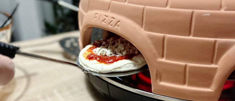 Eine Pizza wird in den Pizzaofen von Heidenfeld eingeschoben.