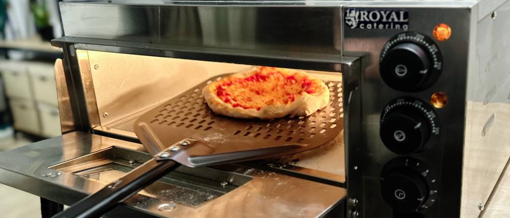 Eine Pizza wird aus dem Pizzaofen von Royal Catering entnommen.