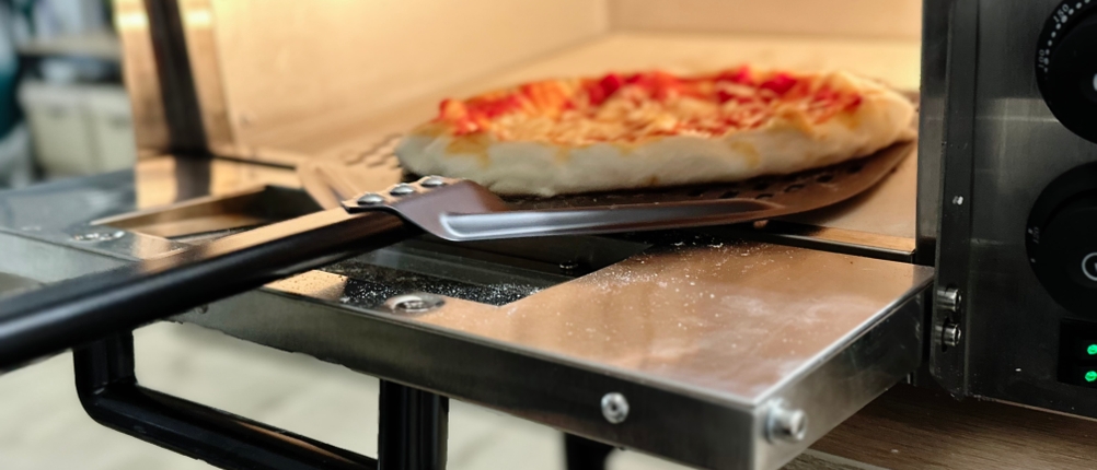 Eine Pizza wird aus dem Pizzaofen von Royal Catering entnommen.