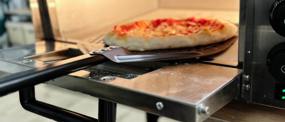 Eine Pizza wird aus dem Pizzaofen von Royal Catering entnommen.