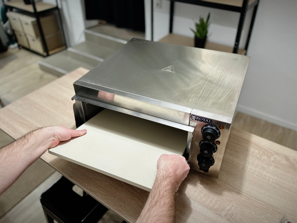 Die Steinplatte wird in den Pizzaofen von Royal Catering eingelegt.