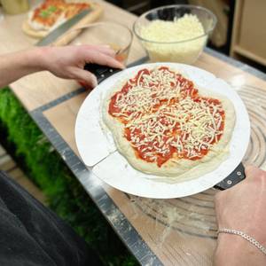 Eine belegte Pizza wird mit einer Schaufel in den G3Ferrari-G1003210-Pizzaofen eingeschoben. Der Deckel ist offen.