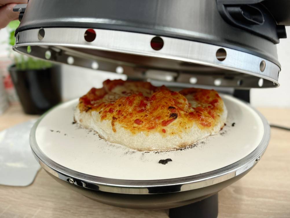Der Deckel des G3Ferrari G1003210 wird langsam geöffnet, die Pizza liegt sichtbar auf dem Pizzastein.