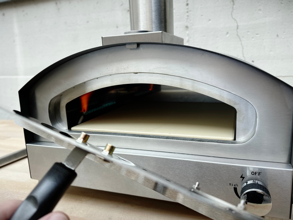 Der Heidenfeld KY019G steht geöffnet und einsatzbereit auf einem Tisch. Der Pizzastein liegt sauber und mittig im Garraum.