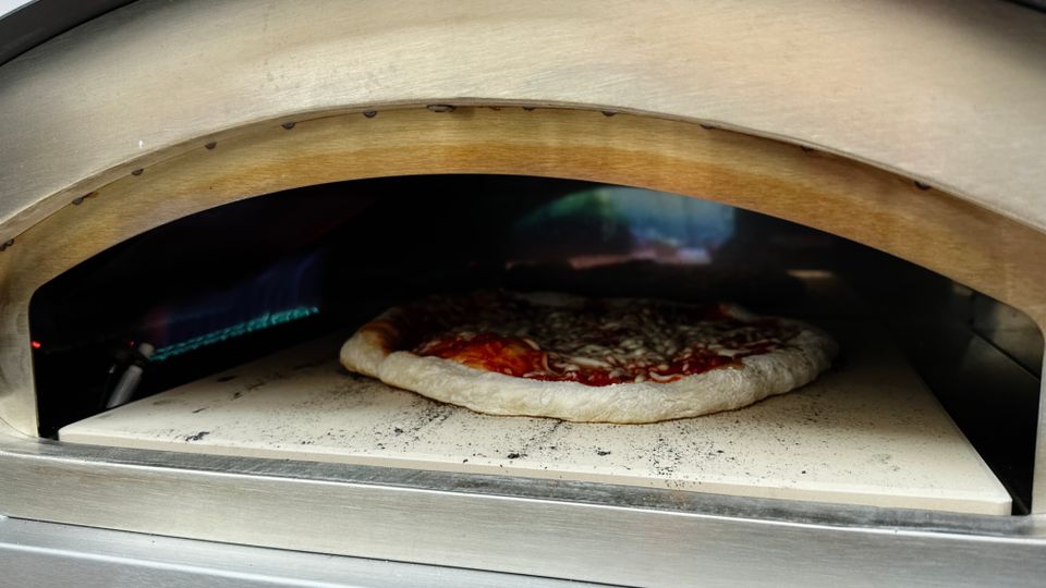 Eine Pizza mit geschmolzenem Käse backt im Heidenfeld KY019G Pizzaofen. Im Hintergrund ist die blaue Gasflamme sichtbar.