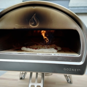 Eine belegte Pizza liegt mittig im Gozney Pizzaofen. Im Hintergrund ist eine kleine Flamme sichtbar.