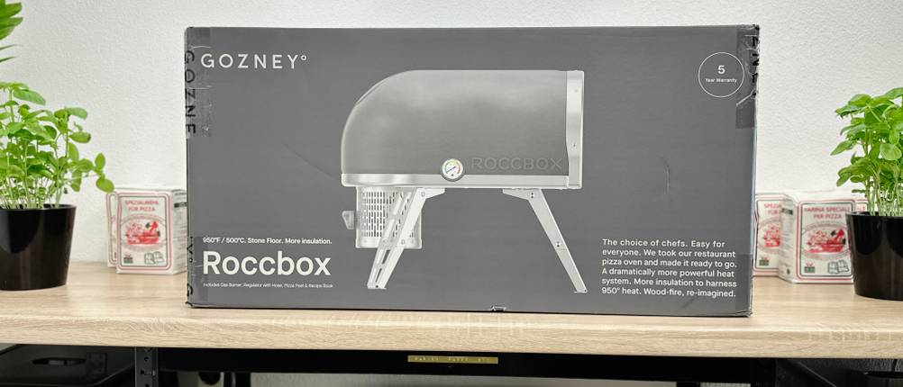 Die Produktverpackung des Gozney Roccbox Pizzaofens zeigt ein Abbild des Ofens mit technischen Daten. Die Verpackung steht auf einem Regalbrett.