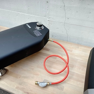 Der Mimiuo-Pizzaofen liegt auf einem Tisch, der rote Gasschlauch ist angeschlossen. Der Regler ist sichtbar.