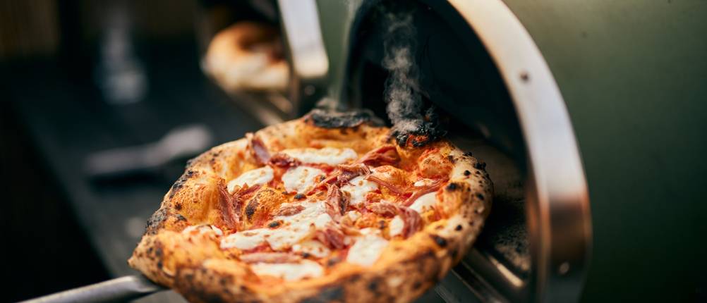 Pizzaofen getestet: Zwei nebeneinander stehende kleine Pizzaöfen mit frisch gebackenen Pizzen.