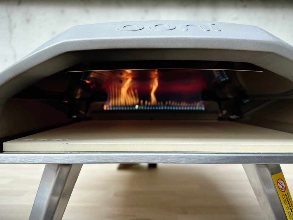Der Ooni Koda 12 ist geöffnet und zeigt den leeren Pizzastein im Garraum. Im Hintergrund brennt die Gasflamme.