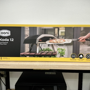 Seitenansicht der Ooni Koda 12 Verpackung mit Abbildung des Ofens im Einsatz. Die Features sind mit Icons hervorgehoben.