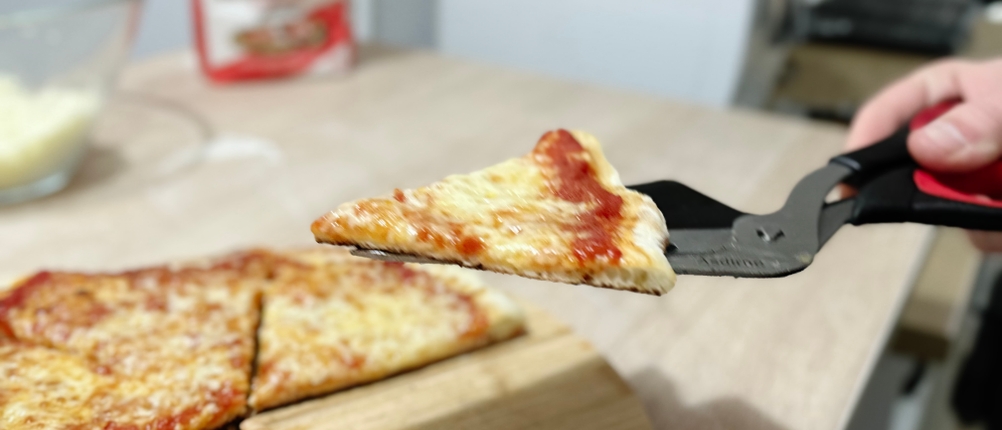 Ein Stück einer geschnittenen Pizza wird mithilfe der Pizzaschere von Asdirne angehoben.