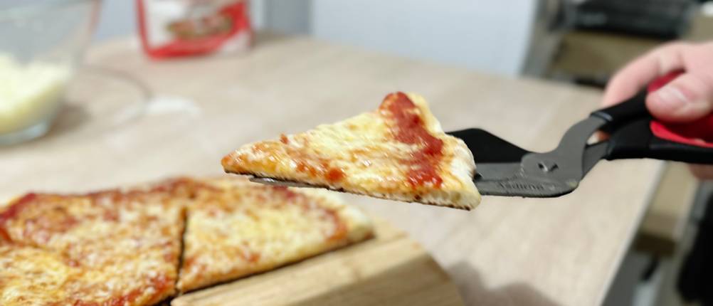 Ein Stück einer geschnittenen Pizza wird mithilfe der Pizzaschere von Asdirne angehoben.