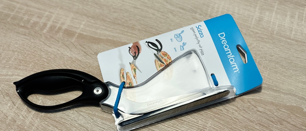 Die Pizzaschere von Dreamfarm liegt eingepackt auf einem Holztisch.