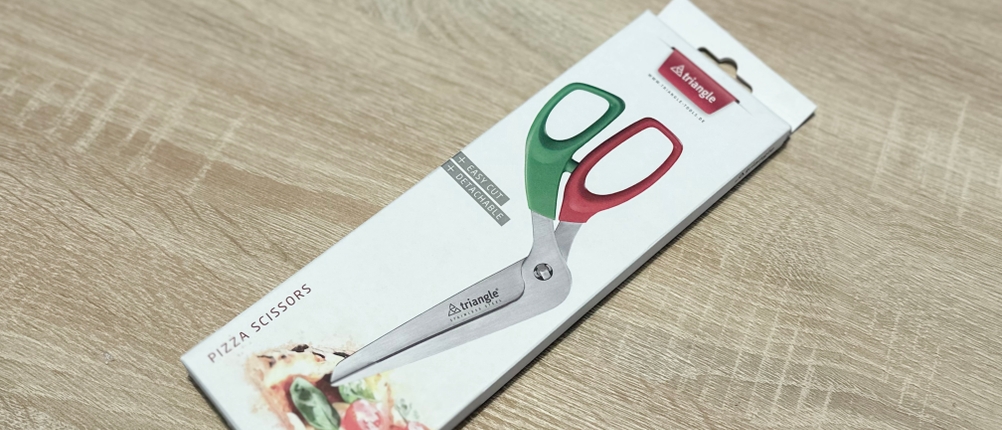 Die Pizzaschere von Triangle liegt eingepackt auf einem Holztisch.