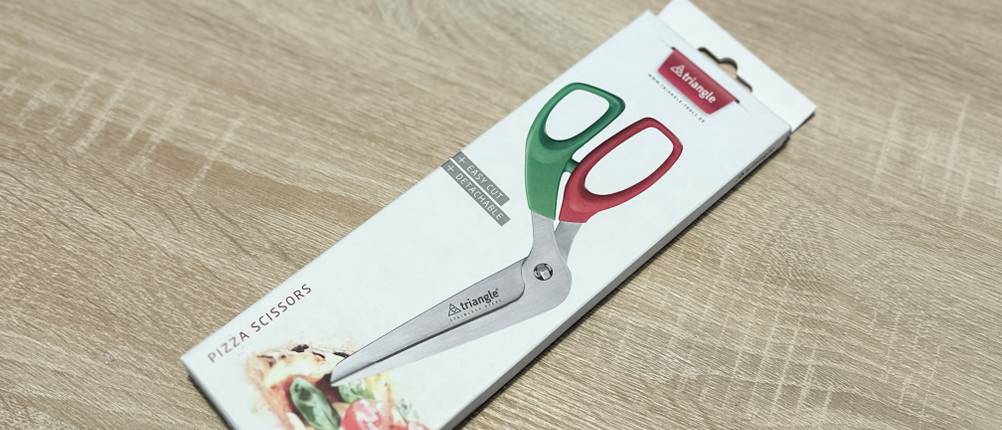 Die Pizzaschere von Triangle liegt eingepackt auf einem Holztisch.