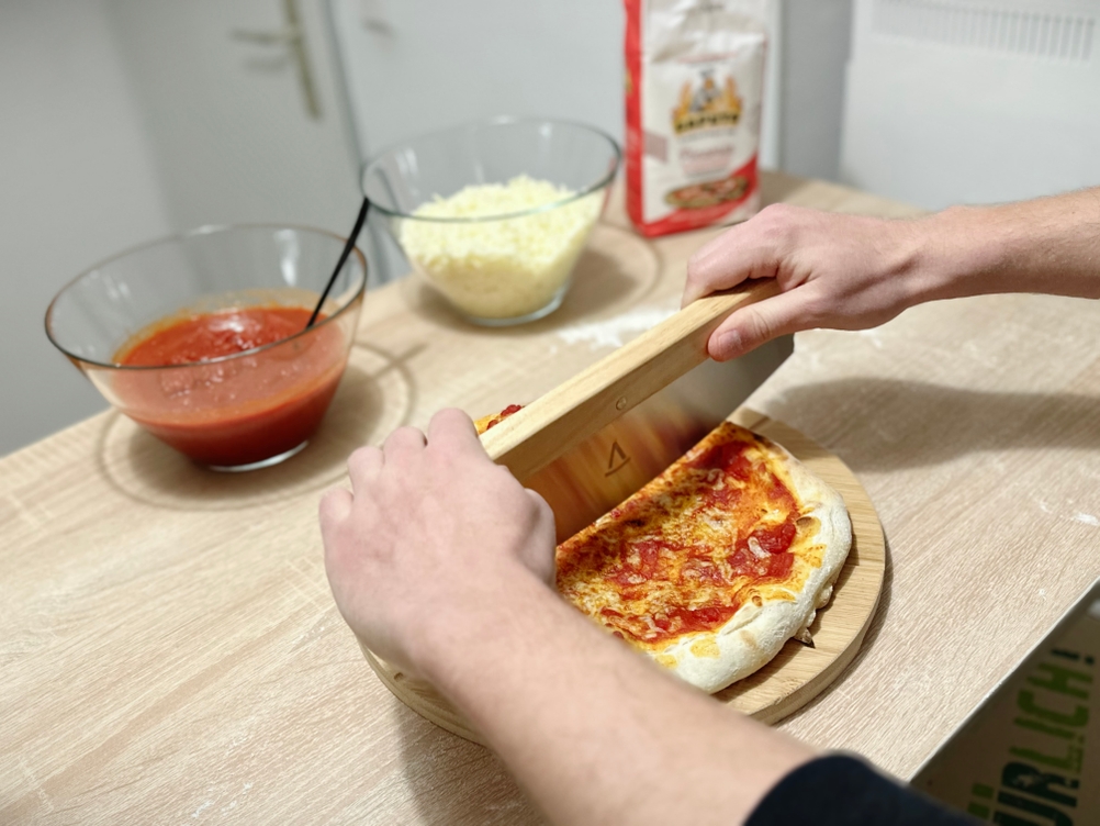 Eine Pizza wird mit dem Pizzaschneider von Pizza Mondo geschnitten.