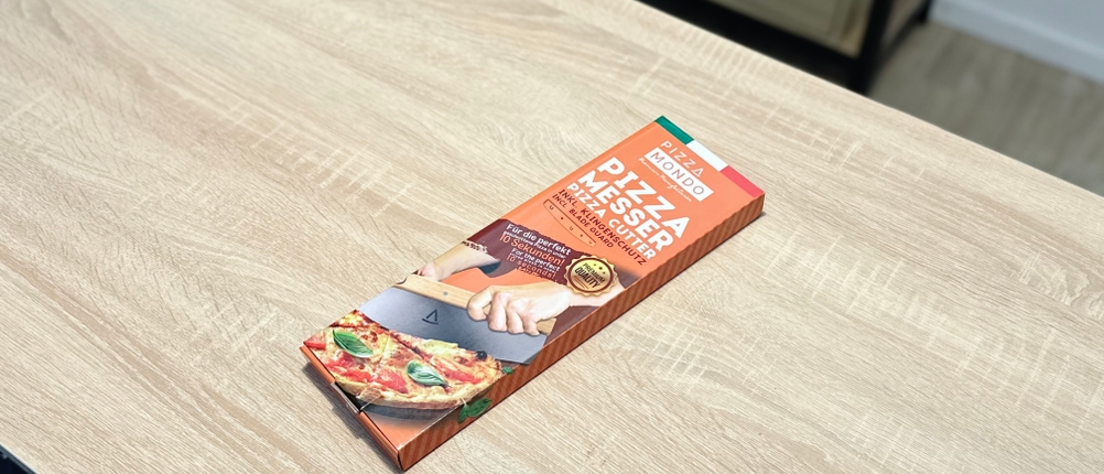 Der Pizzaschneider von Pizza Mondo liegt eingepackt auf einem Holztisch.
