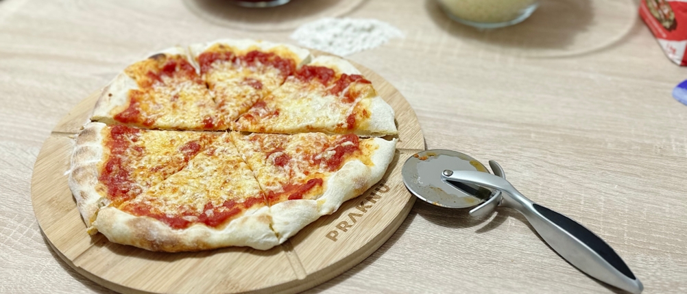 Der Pizzaschneider von Valuxe liegt neben einer Pizza auf einem Holztisch.
