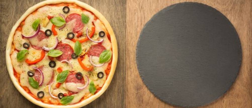 Pizza neben Pizzastein und Zutaten auf Holzfläche.