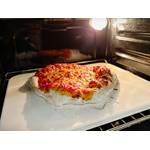 Eine Pizza backt im Ofen auf einem weißen Pizzastein von Blumtal. Der Rand der Pizza ist bereits gut aufgegangen.