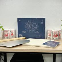 Das komplette Blumtal Set mit Schaufel, Pizzastein und Anleitung liegt auf einem Tisch. Verpackung und Mehl stehen im Hintergrund.