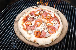 Pizzastein mit Pizza auf einem Grillrost.
