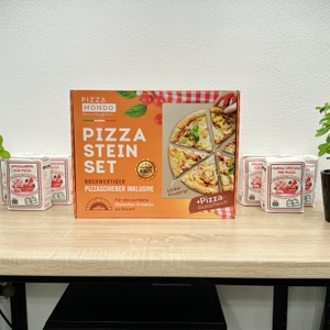 Das Pizza Mondo Pizzastein Set steht aufrecht auf einem Tisch, flankiert von Mehl und Basilikum in Blumentöpfen.
