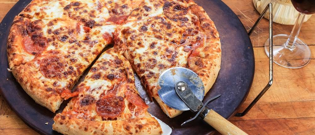 Auf einem Pizzastein liegt eine fertige Pizza mit Pizzaschneider und Tortenheber.