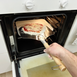 Eine belegte Pizza backt auf einem Pizzastein im Backofen. Der Rand ist bereits leicht aufgegangen.