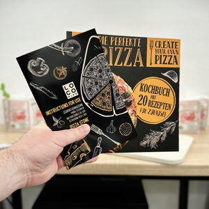 Eine Hand hält ein schwarzes Rezeptbuch und eine Anleitung mit Illustrationen für den Pizzastein von Locbird.