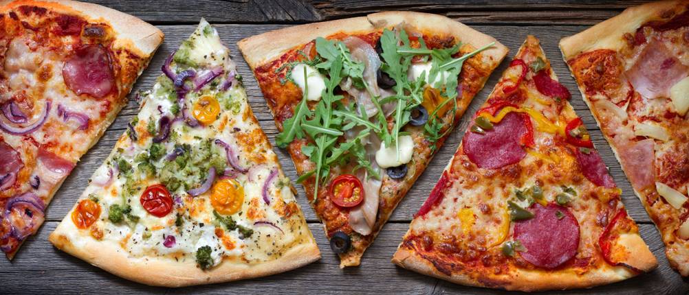 Fünf verschiedene belegte Pizzastücke liegen auf einer Holzoberfläche.