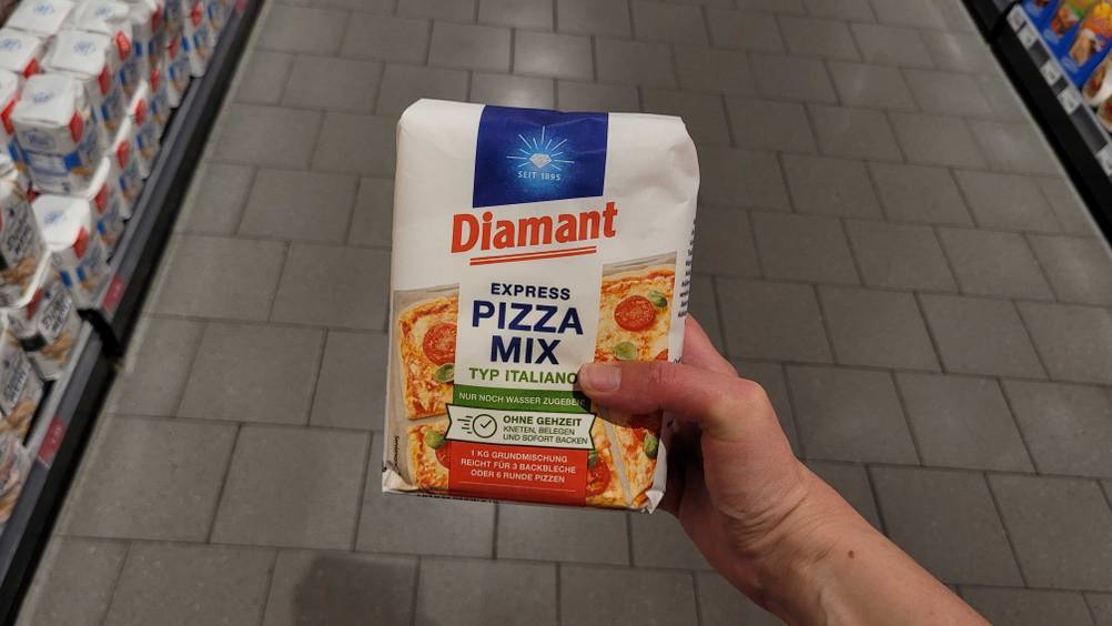 Eine Hand hält eine Packung der getesteten Pizzateig-Backmischung hoch.