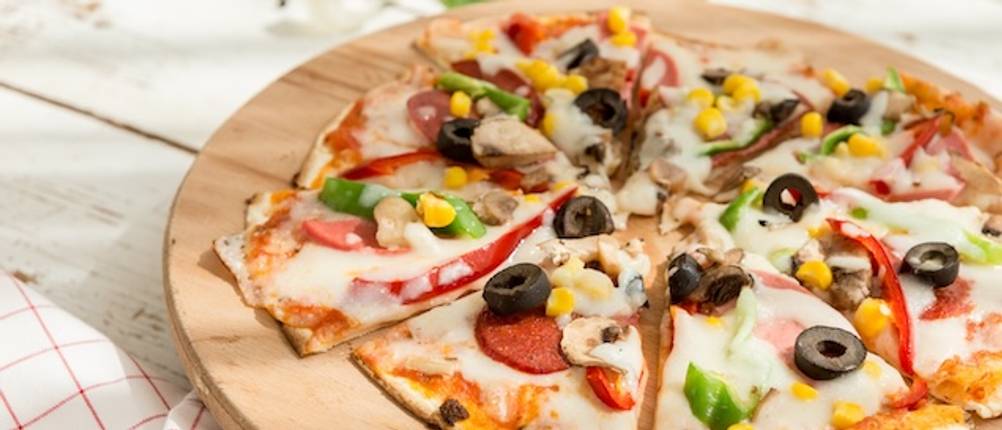 Nahaufnahme eines getesteten Pizzatellers aus Holz mit einer in Stücke geschnittenen dünnen Pizza.