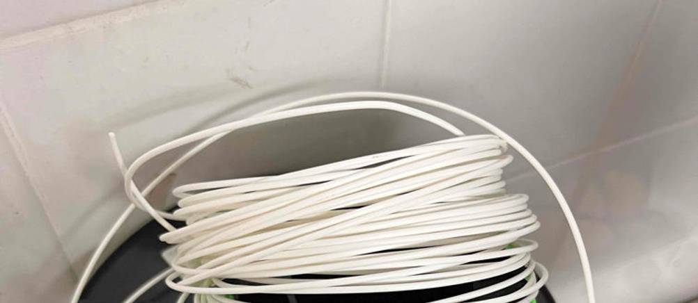 Weißes getestetes 3D-Drucker-Filament liegt lose auf einer Rolle vor weißen Fliesen.