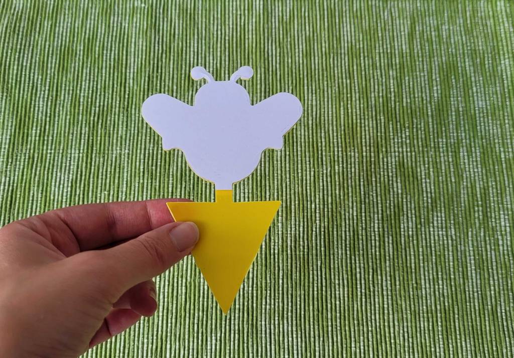 Hand hält getestete Fliegenfalle mit Klebesubstanz vor einem grünen Hintergrund.