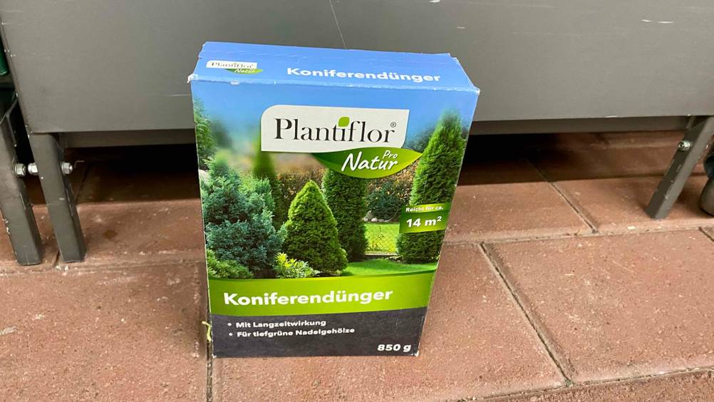 Koniferendünger getestet: Eine Packung auf einem roten Steinboden vor einem grauen Regal.