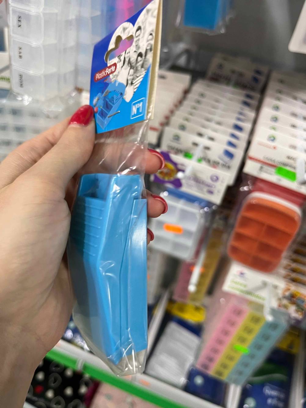 Getestet: Eine Hand hält einen verpackten Tablettenteiler seitlich vor ein Regal.